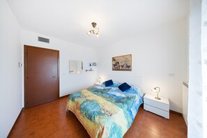A bedroom with a bed, a nightstand, a lamp, a painting on the wall, and a door. - Villa in a residence with swimming pool for 6 people (Polpenazze del Garda)