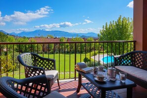 A balcony with wicker furniture, a table with a book, cups, and a teapot, overlooking a swimming pool and green landscape with mountains in the background. - Villa in a residence with swimming pool for 6 people (Polpenazze del Garda)