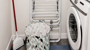 Un cuarto de lavandería con lavadora, un tendedero, una mopa y una cesta de ropa.
