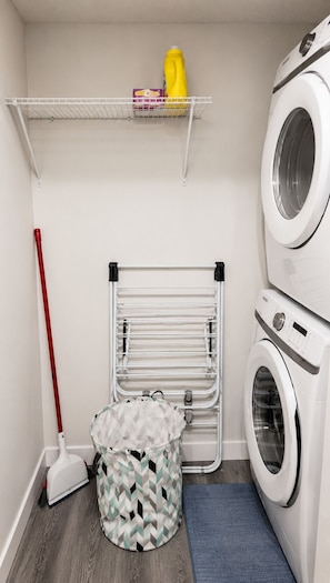 A laundry room with a washing machine, a drying rack, a mop, and a laundry basket.