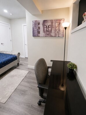 A bedroom with a bed, a desk, a chair, a floor lamp, and a painting on the wall. - Newly Furnished Private Suite | Separate Entry, Kitchen, Laundry & Workspace (Regina)