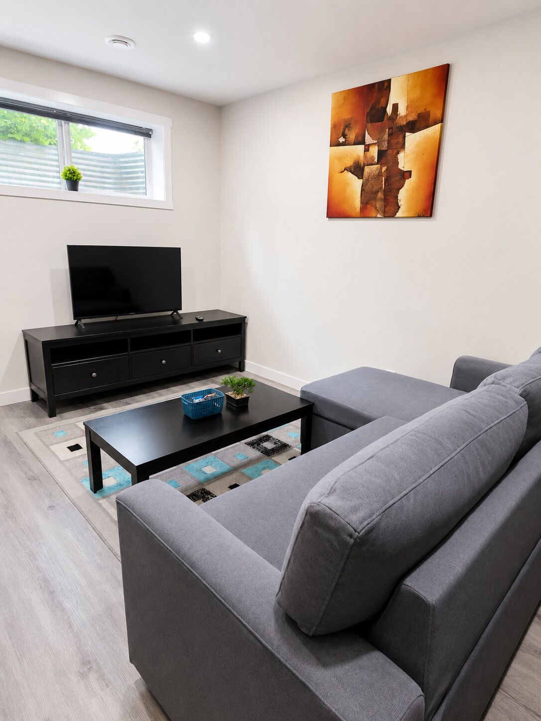 A modern living room with a grey sofa, a black entertainment unit, and a flat-screen TV.