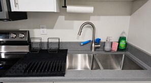 Une cuisine équipée d’un évier en acier inoxydable, d’une cuisinière encastrée et d’un plan de travail avec un égouttoir et des produits de nettoyage.