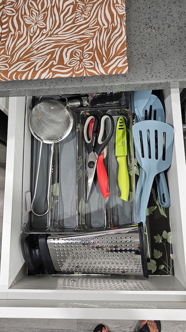 A drawer with kitchen utensils including a strainer, scissors, a grater, and a spatula. - Newly Furnished Private Suite | Separate Entry, Kitchen, Laundry & Workspace (Regina)
