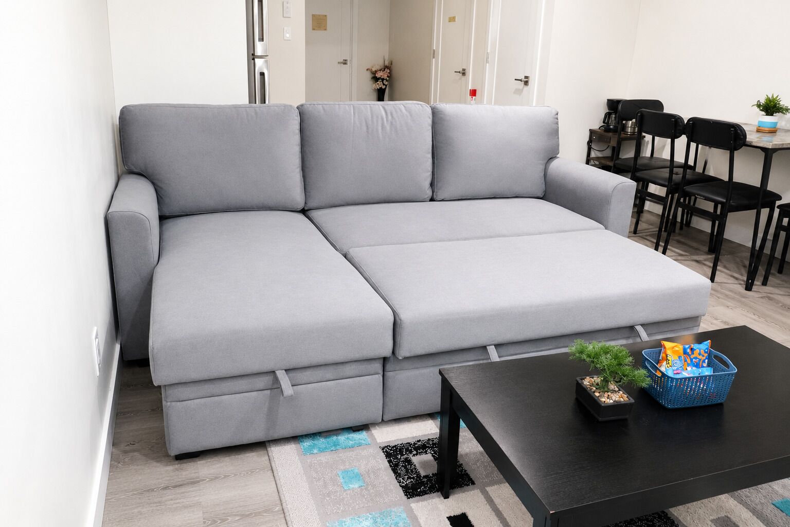 En grå, modulbaserad soffa i ett modernt vardagsrum, tillsammans med ett svart soffbord, en blå korg och en liten växt.
