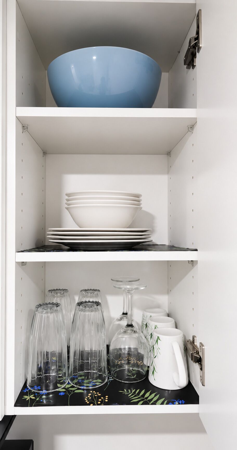 A kitchen cabinet with shelves holding a blue bowl, stacked plates, and glassware.