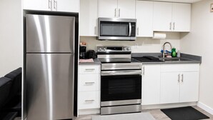 Una cocina moderna con electrodomésticos de acero inoxidable, armarios blancos y encimera negra.