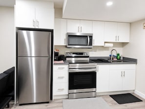A modern kitchen with stainless steel appliances, white cabinets, and a black countertop.