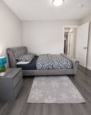 Een slaapkamer met een bed, nachtkastjes, een lamp en een deur.