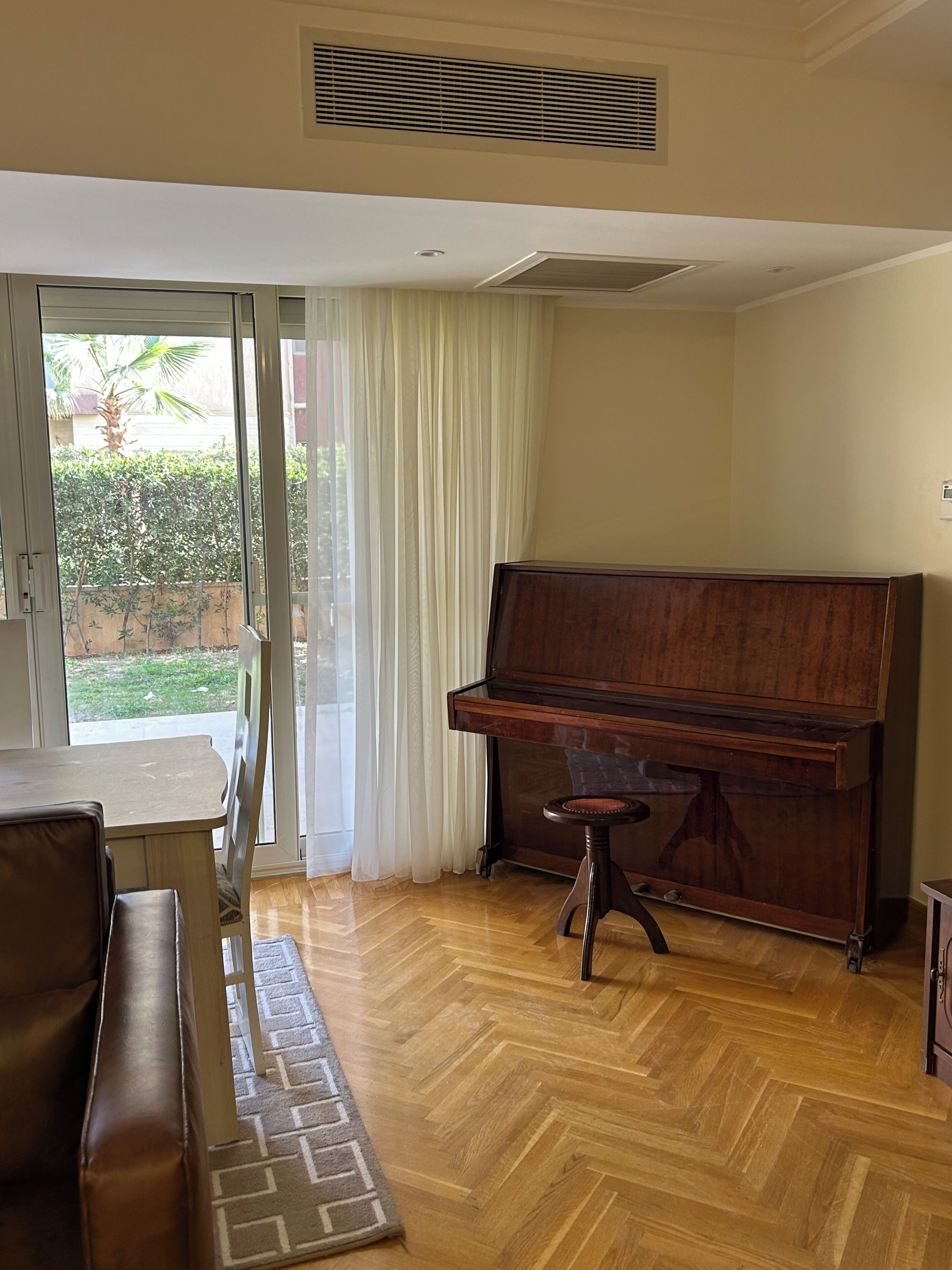 Uma sala de estar com um piano, um sofá, uma mesa de jantar e vista através de uma porta de vidro.