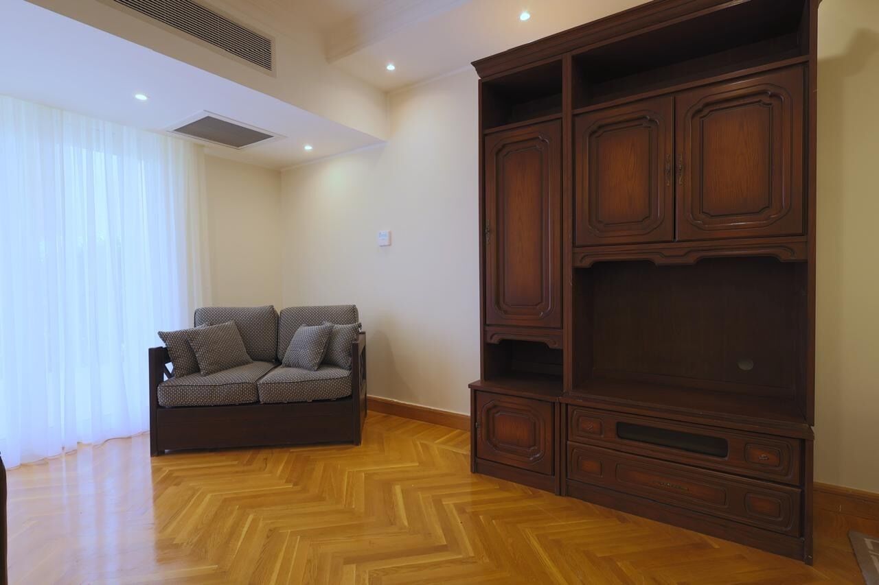 Un salón con suelo de madera tipo espiga, un sofá marrón oscuro con cojines estampados y un mueble de madera grande con varios cajones.
