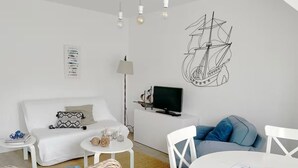 Ein modernes Wohnzimmer mit einem weißen Sofa, einem Esstisch und einem Fernseher auf einem Lowboard.