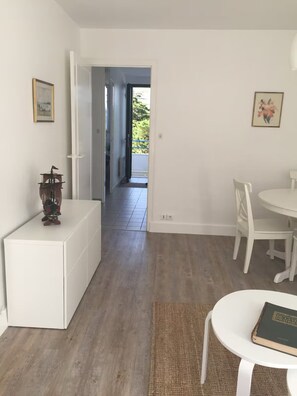 A room with a white cabinet, a small table with a book, and a chair. There is a door leading to a balcony with a view of greenery. - T3 4/6p Side sea view Terrace 30m from the Beach (La Baule-Escoublac)