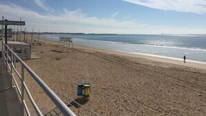 Ein Strand mit einem Rettungsturm, blauem Himmel und einer Person, die am Sand entlanggeht.
