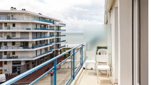 Ein mehrstöckiges Gebäude mit Balkonen und Blick auf das Meer, auf dem Balkon befindet sich ein weißer Stuhl.