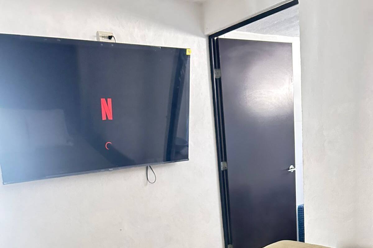 A bedroom with a bed, a remote control, a TV mounted on the wall, and a door.