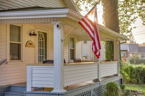 A white house with a porch, a flag, and a small garden.