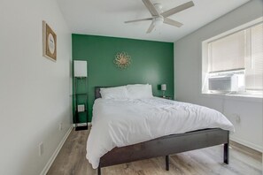 A bedroom with a bed, a ceiling fan, a window with blinds, and a green accent wall.