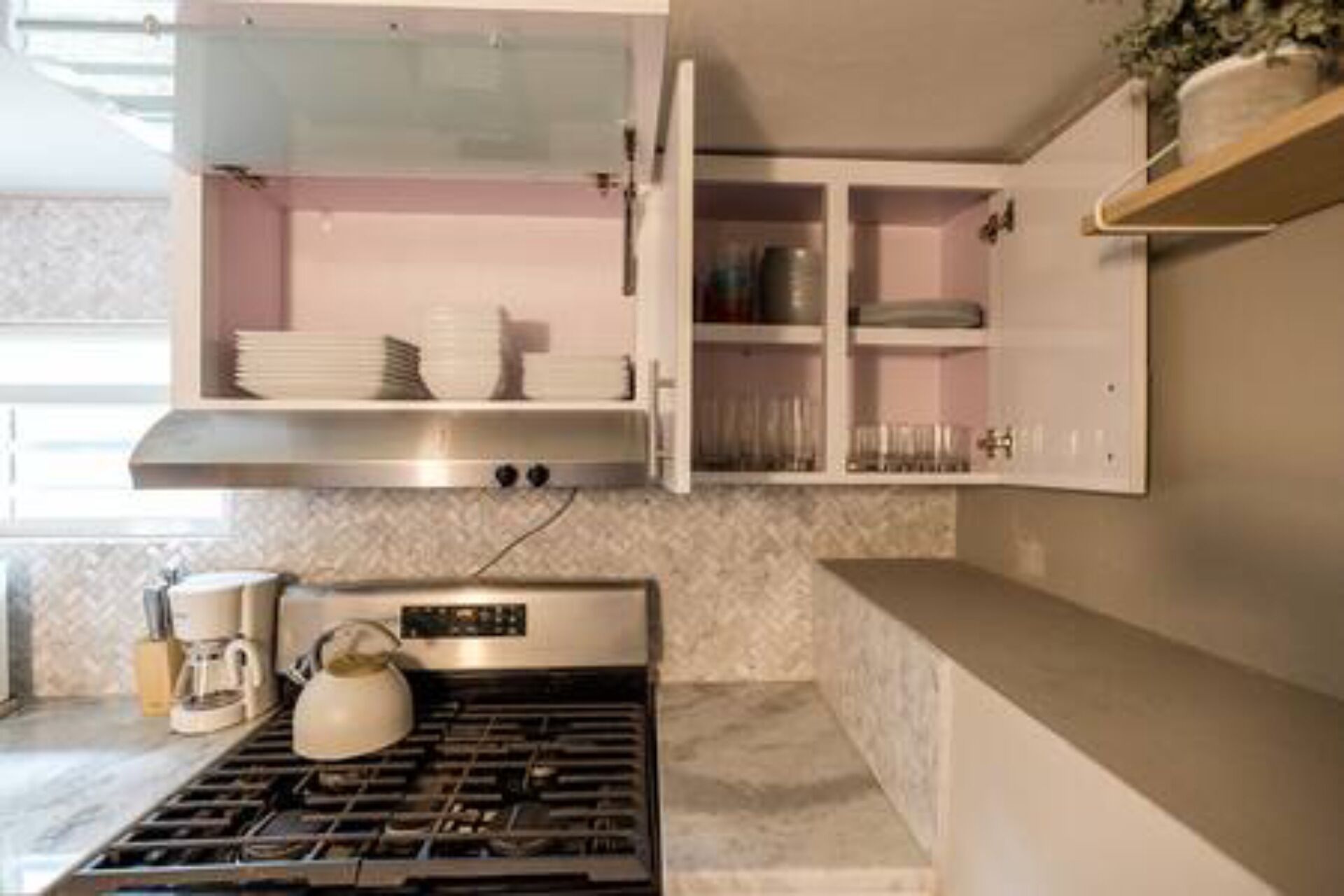 Een moderne keuken met een gasfornuis, een waterkoker en open kastjes met servies en glazen.