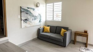 A living room with a grey sofa, yellow cushions, a wooden side table, and a large abstract painting on the wall.