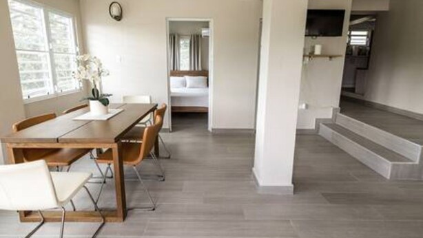 A spacious living area with a wooden dining table, white chairs, and a large window.