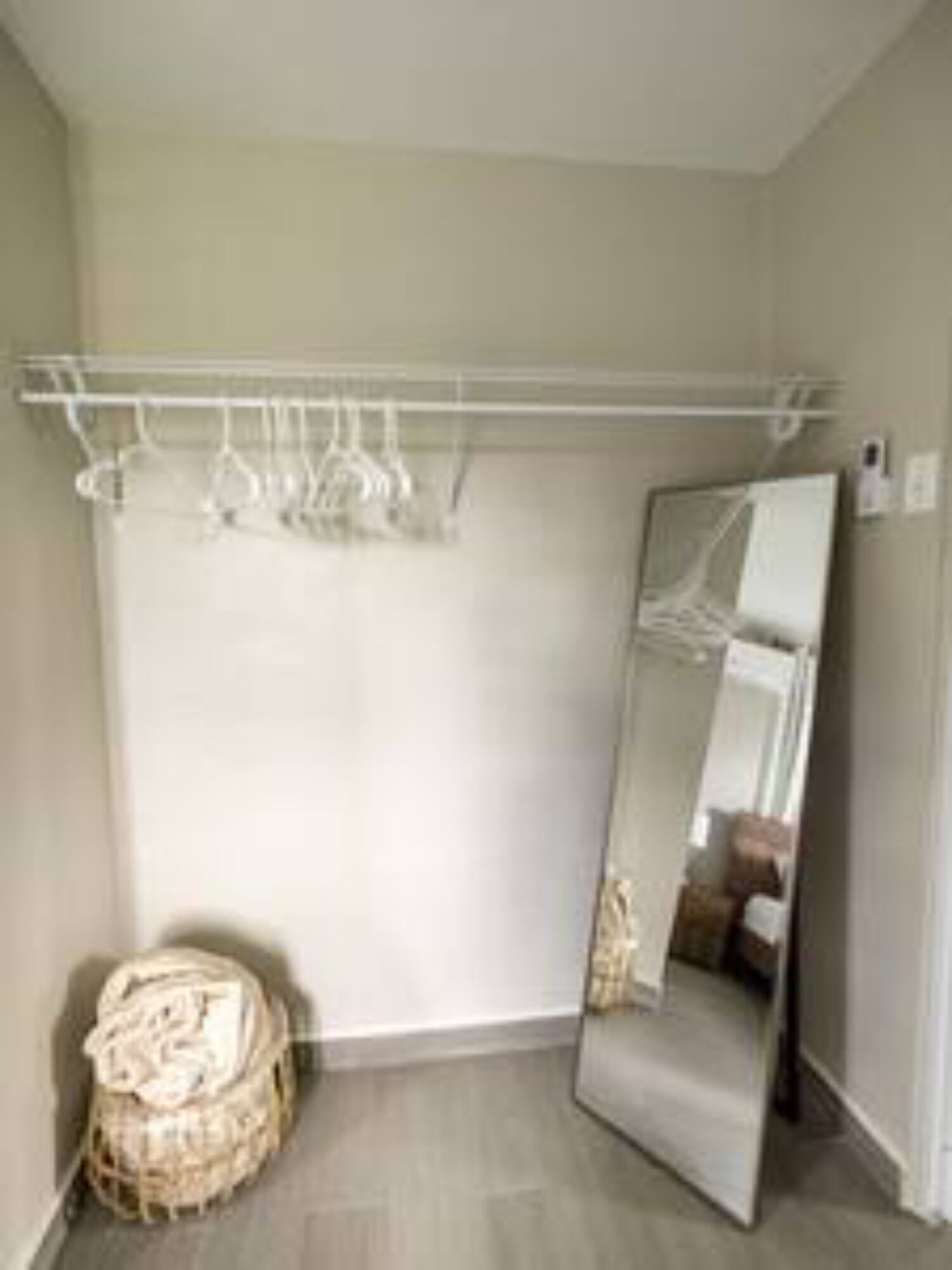 Una habitación con un espejo grande, un armario blanco con barra para colgar ropa y una cesta de mimbre.
