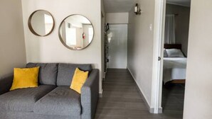 Una habitación de hotel con un sofá gris, dos espejos redondos en la pared y una cama con ropa blanca.