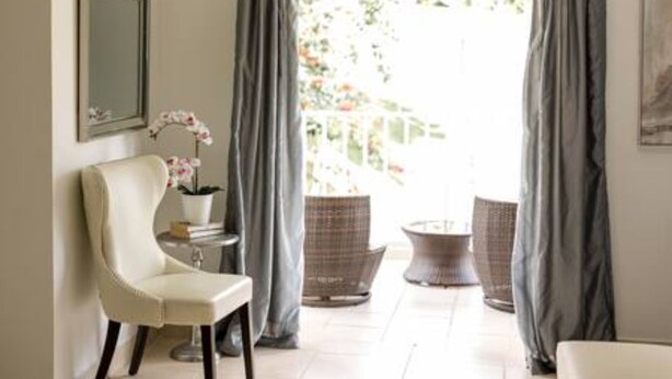 Ein Zimmer mit einem weißen Stuhl, einem kleinen Tisch mit Orchidee im Topf und zwei Korbstühlen.