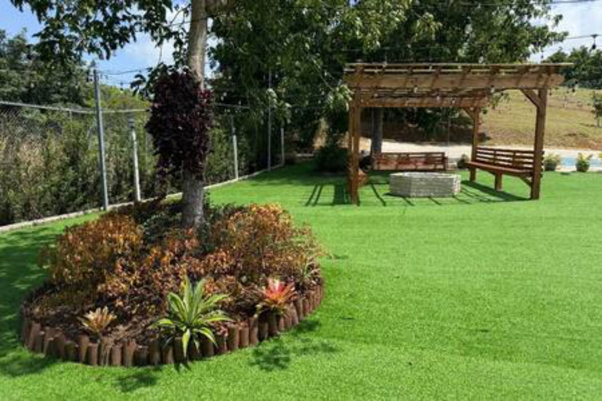 A well-maintained garden with a wooden pergola, a tree, and a grassy lawn.