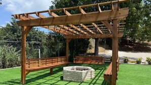A wooden pergola structure with a stone fire pit in the center, surrounded by a well-maintained lawn. - Reposo at Hacienda el Lago (Cayey)