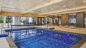 Piscina interior com teto de madeira, cadeiras de descanso e vista para o exterior.