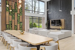 A modern interior with a long dining table, multiple chairs, a sofa, and a flat-screen TV mounted on a textured wall. - New Modern Creekfront Mansion with Indoor Pool and Sauna by Camelback (Tannersville)