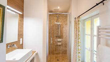 Une salle de bain avec une douche en verre, un lavabo, un miroir et une fenêtre avec un porte-serviettes.