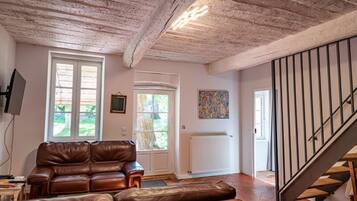 Un salon avec un canapé en cuir marron, un téléviseur, une fenêtre, une porte, un radiateur et un escalier.