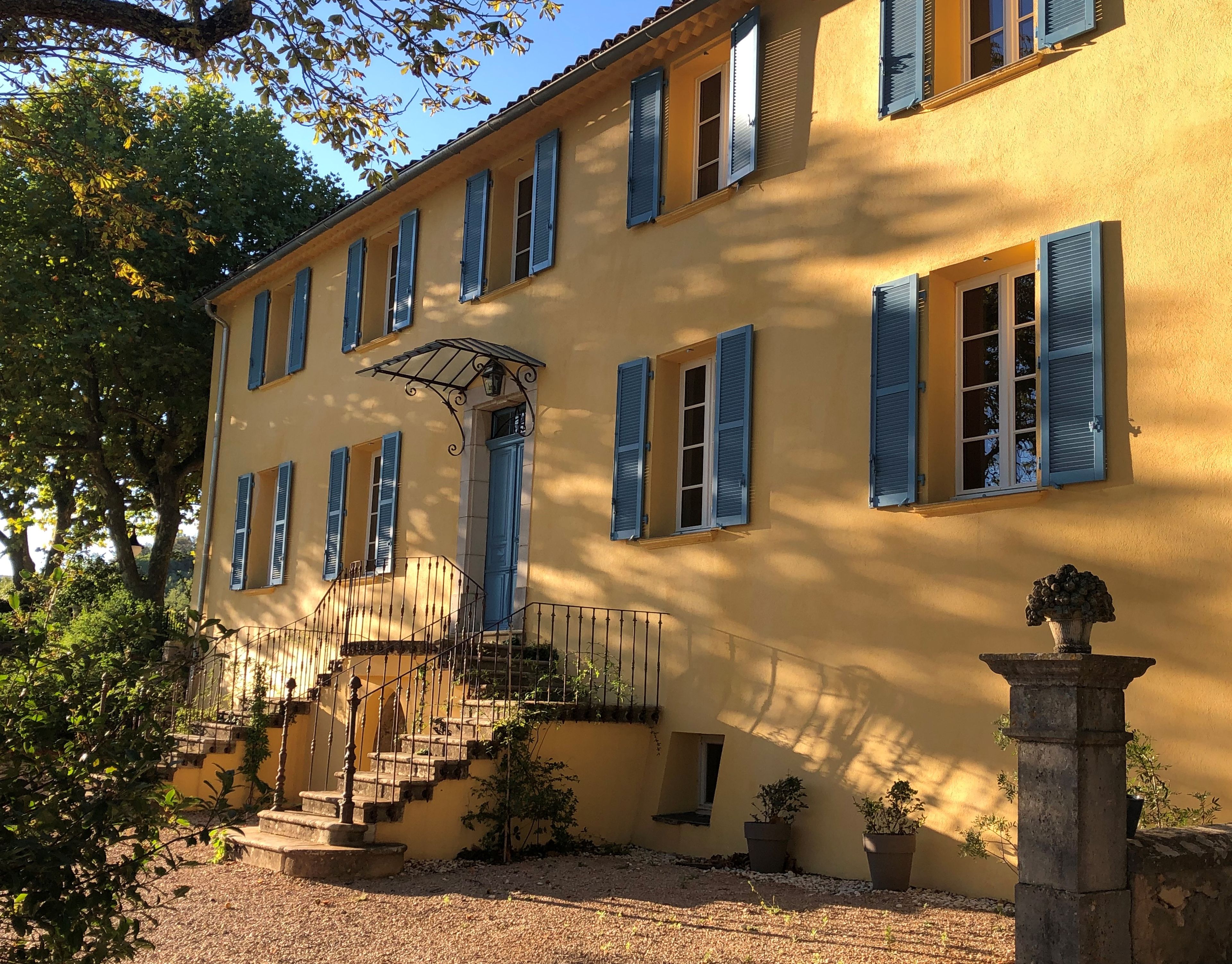 A yellow building with blue shutters, a staircase, and a stone pillar.