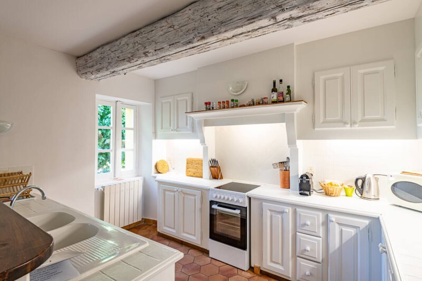 A kitchen with white cabinetry, a built-in oven, a stove, and a window with a view of greenery.