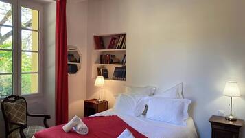 A hotel room with a bed, a bookshelf, a chair, and a window with curtains.