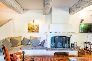 A cozy living room with a fireplace, a sofa with cushions, a television, and a painting on the wall. - Château de Trians – 3 Pools, 19 Bedrooms, Sleeps up to 48 (Néoules)