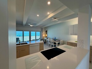Een moderne keuken met een centraal eiland, een eethoek met stoelen en uitzicht op de oceaan door grote ramen.