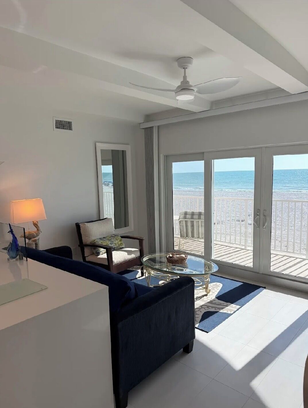 Ein modernes Wohnzimmer mit einem großen Glasfenster, das auf einen Balkon mit Blick zum Strand führt.