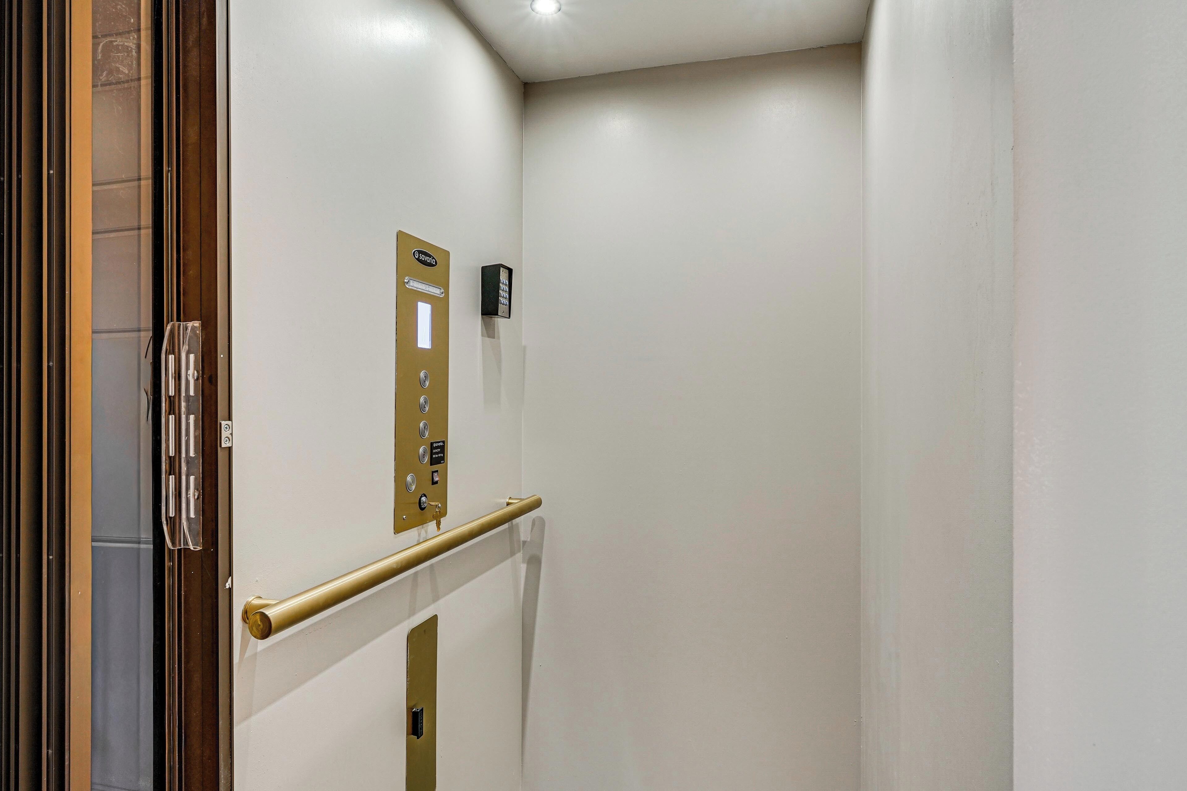 Un pasillo estrecho con una puerta a la izquierda, un panel de control en la pared y una barandilla.