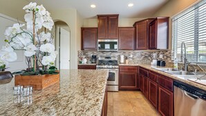 A modern kitchen with granite countertops, stainless steel appliances, wooden cabinets, and a large window with blinds. - Sophisticated Sanctuary: 8 Mi to Lodi Wineries! (Stockton)
