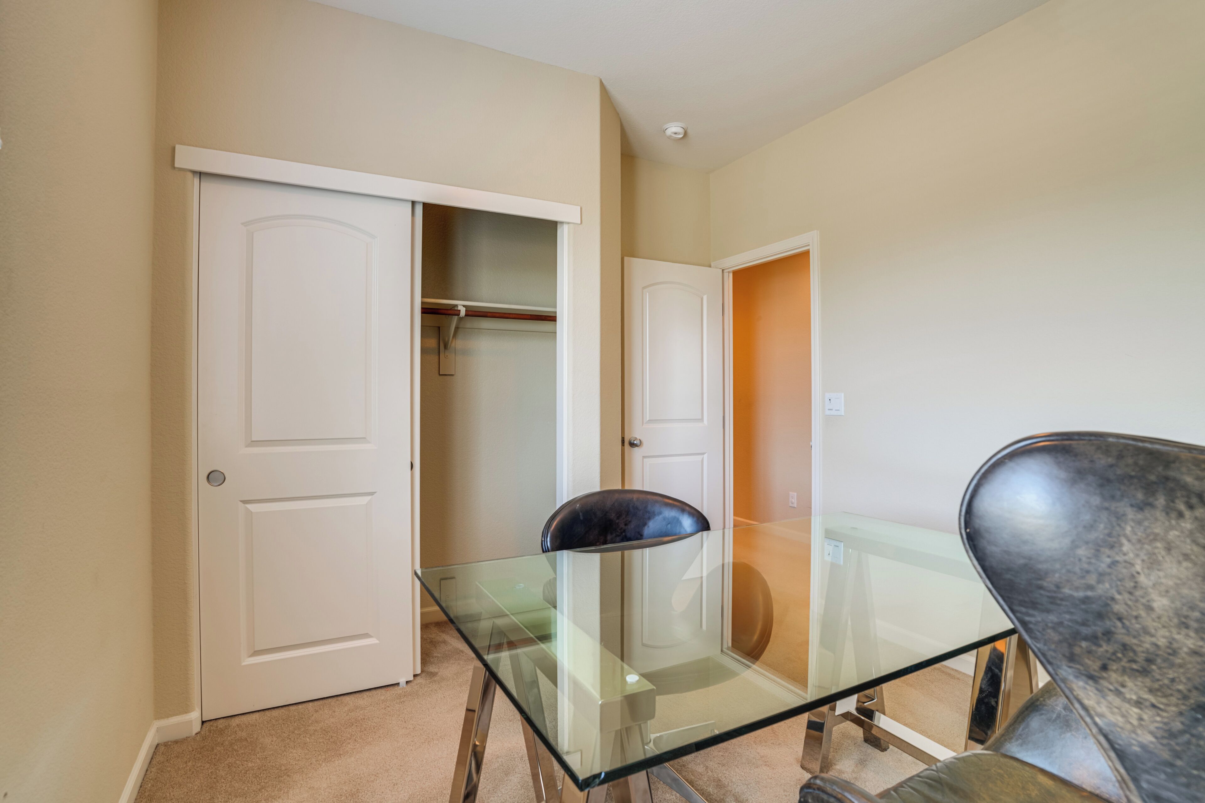 A room with a glass-top table, a chair, and a closet with hanging clothes.