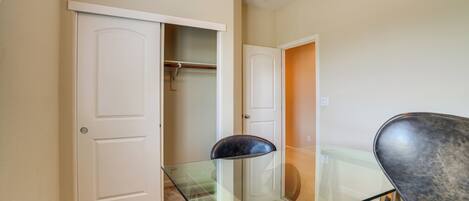 A room with a glass-top table, a chair, and a closet with hanging clothes.