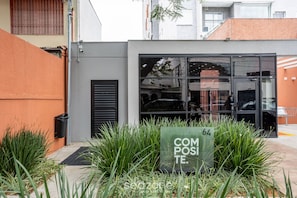 A building with a glass entrance, a green sign with the number 64, and a garden area with tall grass. - Apt w/ Balcony 350m From Shopping Ecg1308 (São Paulo)