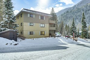 Ein mehrgeschossiges Gebäude mit verschneitem Gelände, umgeben von Bäumen und Bergen.