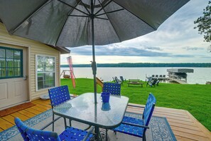 En udendørs terrasse med et bord og stole, en stor parasol og udsigt til en sø.