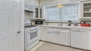 A kitchen with white cabinets, a stove, a microwave, a sink, and a window with blinds. - Shop, Dine & Explore: Home 3 Mi to NRG Stadium (Houston)