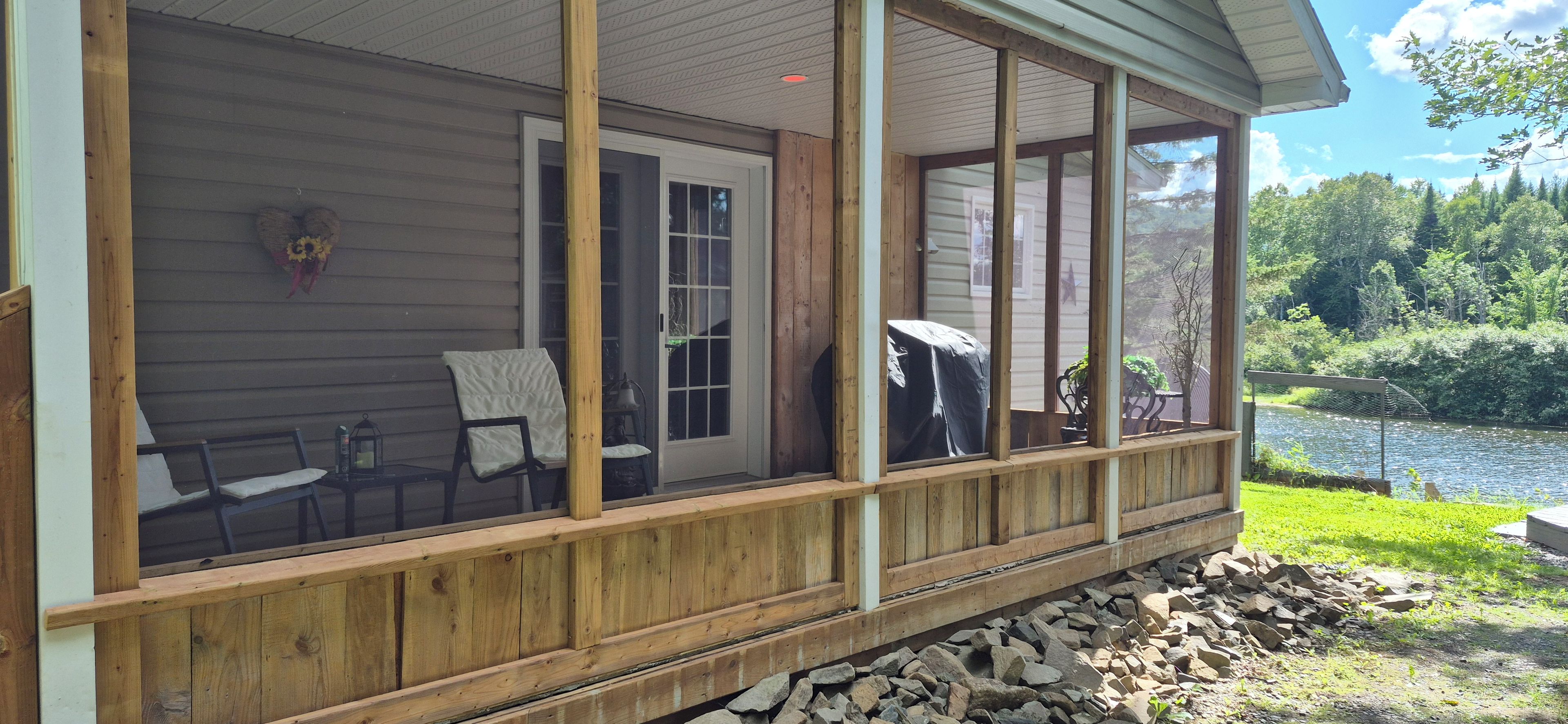 A wooden deck with a covered area, a chair, a table, and a view of a lake.