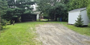 A gravel driveway leading to a wooden gate, surrounded by lush greenery and a small shed.